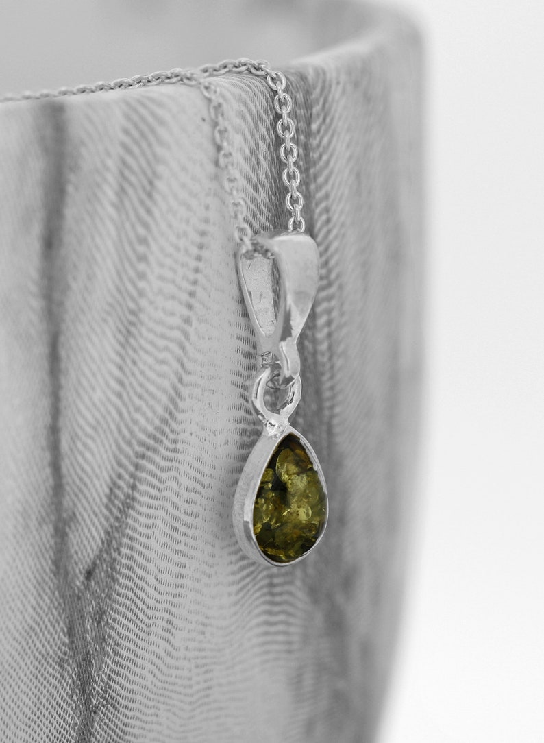 May include: A silver chain necklace with a teardrop-shaped pendant featuring a green amber stone.