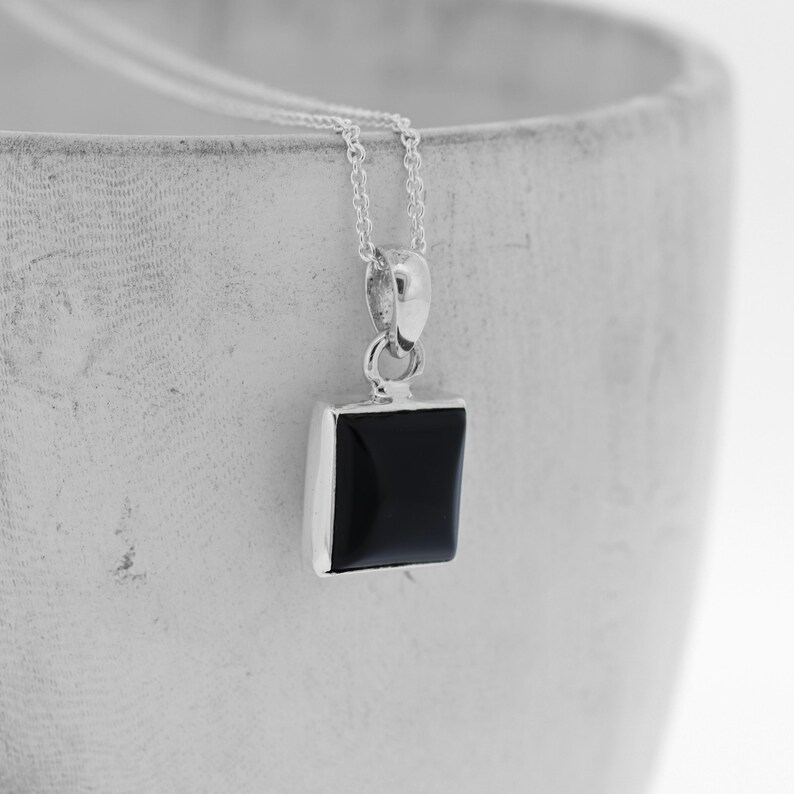 Puede incluir: Un collar de cadena de plata con un colgante cuadrado de &oacute;nix negro.