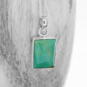 May include: A silver chain necklace with a turquoise pendant. The pendant is rectangular in shape with a smooth, polished surface.