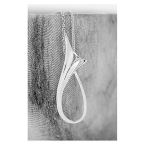 May include: A silver pendant necklace featuring a distinctive, abstract design. The pendant is shaped like a teardrop with a curved, flowing line.