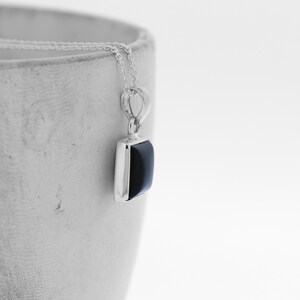 Puede incluir: Un collar de cadena de plata con un colgante cuadrado de &oacute;nix negro.