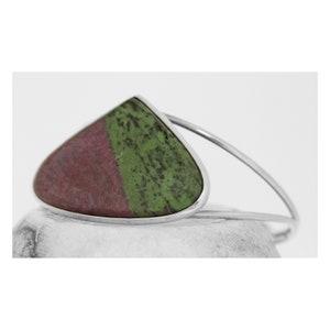 May include: A silver bangle bracelet featuring a teardrop-shaped green and pink gemstone.