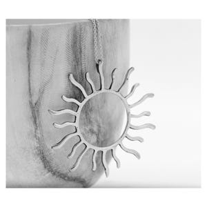 Peut inclure: Un collier avec un pendentif soleil argenté. Le soleil a un centre circulaire avec des rayons rayonnants. Le collier est suspendu à une chaîne délicate. Le fond est une surface texturée et claire.