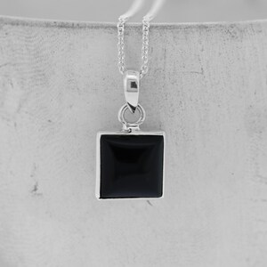 Puede incluir: Un collar de cadena de plata con un colgante cuadrado de &oacute;nix negro.