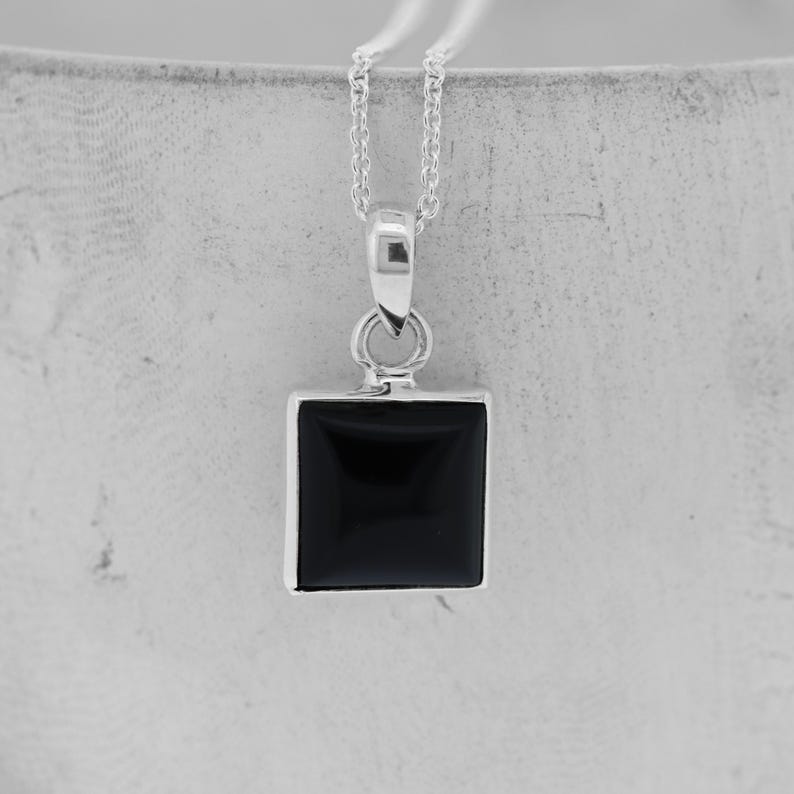 Puede incluir: Un collar de cadena de plata con un colgante cuadrado de &oacute;nix negro.