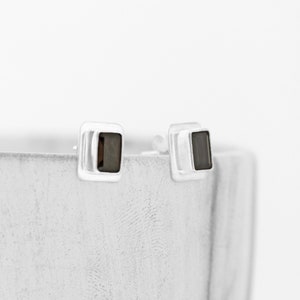 May include: A pair of silver square stud earrings with black square stones.