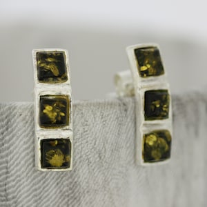 May include: A pair of silver earrings with three green amber stones in each earring.