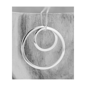 Puede incluir: Un collar de plata con dos círculos entrelazados. Los círculos son lisos y tienen un acabado pulido.