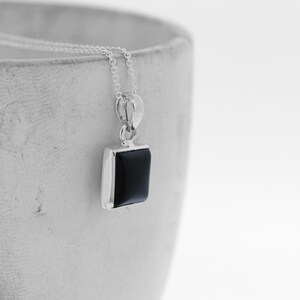 Puede incluir: Un collar de cadena de plata con un colgante cuadrado de &oacute;nix negro.