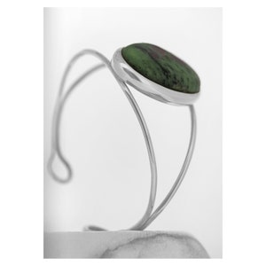 Puede incluir: Un brazalete de plata con una piedra ovalada verde engastada en un bisel de plata.