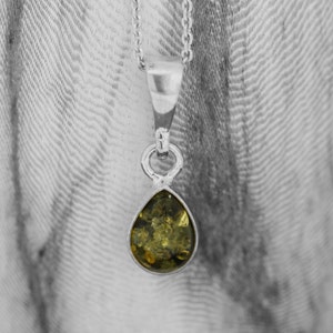 May include: A silver pendant necklace with a teardrop-shaped green amber stone.