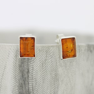 May include: A pair of silver stud earrings with square amber stones.