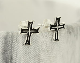 May include: A pair of silver cross stud earrings with black enamel accents.