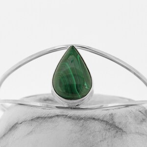 May include: A silver bangle bracelet with a teardrop-shaped malachite stone in the center.