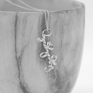 Peut inclure: Un collier en argent avec un pendentif délicat en forme de branche torsadée. Le pendentif présente plusieurs petites feuilles ovales.