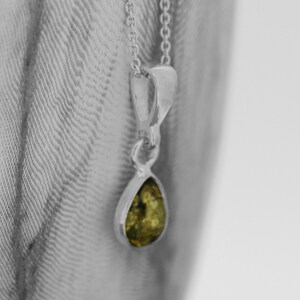 May include: A silver chain necklace with a teardrop-shaped pendant featuring a green gemstone.