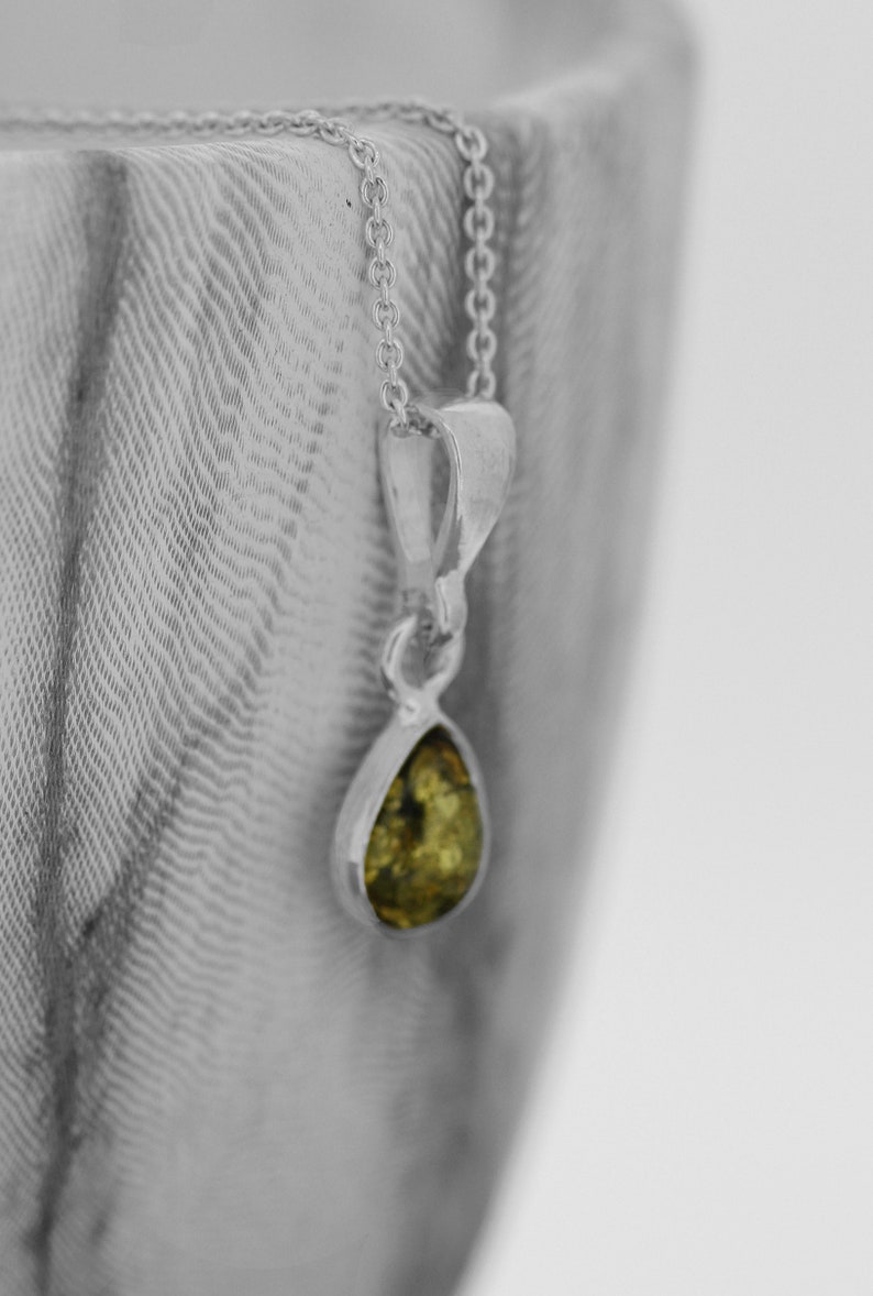 May include: A silver chain necklace with a teardrop-shaped pendant featuring a green gemstone.
