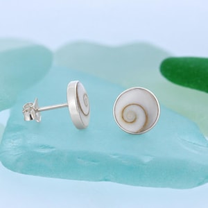 May include: A pair of round stud earrings featuring a natural white and brown spiral shell pattern set in a polished silver-toned metal frame. One earring is shown from the side displaying the post and butterfly back, while the other faces forward.