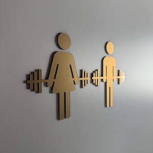 May include: Gold metal silhouette of a person lifting a barbell, with a second silhouette of a person lifting a barbell to the right.