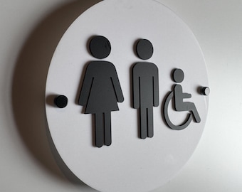 May include: A circular white sign featuring three raised black icons: a stylized figure in a dress, a stylized figure in trousers, and a person in a wheelchair. The sign is mounted with two small black circular fasteners on the left and right sides.