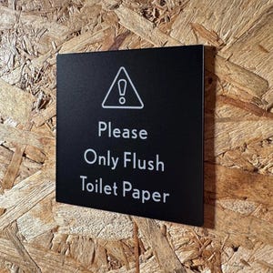 May include: Black sign with a white warning triangle and exclamation point. The sign reads "Please Only Flush Toilet Paper."
