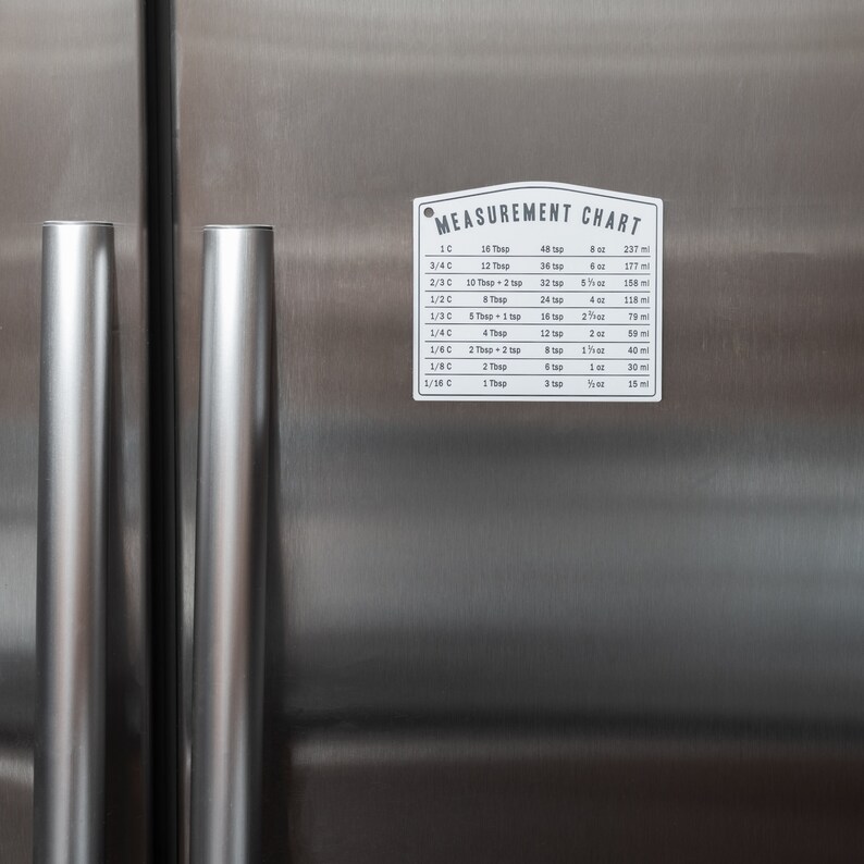 Puede incluir: Un gr&aacute;fico de metal blanco con el texto "MEASUREMENT CHART" impreso en negro. El gr&aacute;fico enumera las medidas equivalentes para tazas y cucharadas en onzas y mililitros.