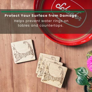 May include: A set of four square light-colored wooden coasters featuring a dark brown laser-engraved map of Cape Cod. The coasters are arranged in a stack and a single piece, positioned near a red circular metal tray with the text Schaefer.