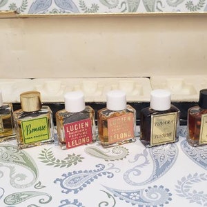 Puede incluir: Un conjunto de diez frascos de perfume en miniatura en una caja negra y blanca. Los frascos están dispuestos en dos filas de cinco. Los frascos son de diferentes colores y tienen diferentes etiquetas. Las etiquetas incluyen los nombres de los perfumes, como "Insolence", "Tubereuse" y "Romanse".