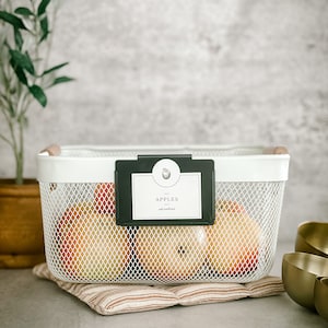 May include: White wire mesh basket with black label that says "APPLES all natural" and filled with red apples. The basket is sitting on a brown and white striped fabric mat.
