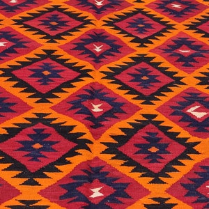 May include: A colorful rug with a geometric pattern in shades of orange, red, black, and blue. The rug has a fringe border.