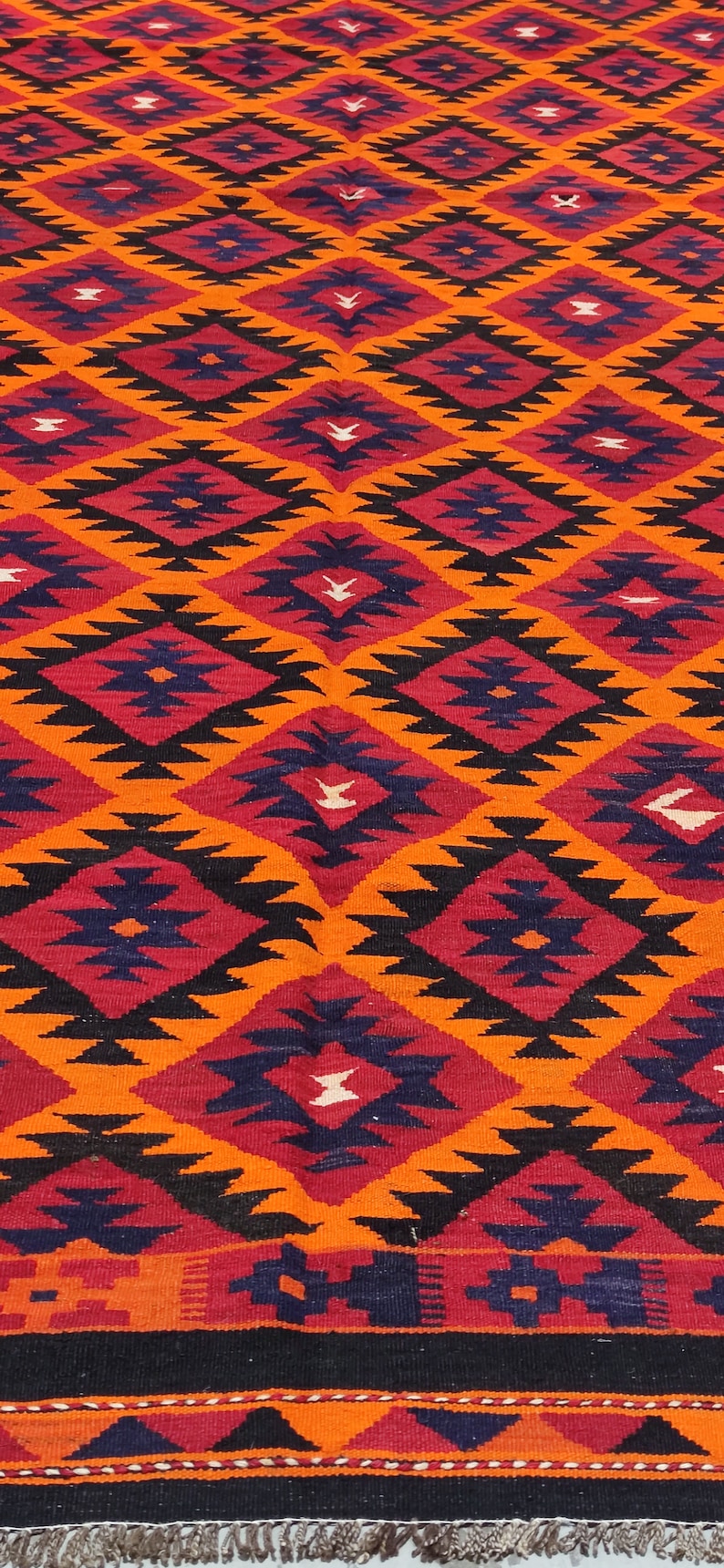 May include: A colorful rug with a geometric pattern in shades of orange, red, black, and blue. The rug has a fringe border.