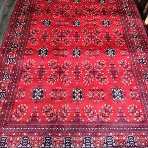 May include: A red rug with a traditional Persian design. The rug has a dark blue border with intricate patterns and a central field with repeating floral motifs.