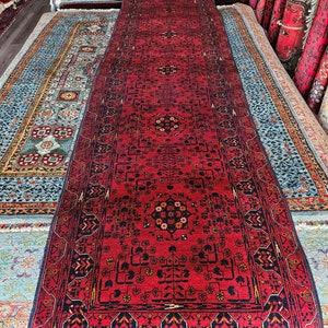 Könnte beinhalten: Ein roter Läuferteppich mit traditionellem persischem Design. Der Teppich hat einen schwarzen Rand und komplizierte Blumenmuster in der Mitte.