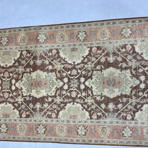 Könnte beinhalten: Ein rechteckiger Teppich mit einem komplizierten Blumenmuster in Braun-, Beige- und Pfirsichtönen. Der Teppich hat ein zentrales Medaillon-Design und einen Rand mit sich wiederholenden Blumenmotiven. Die Textur des Teppichs wirkt weich und einladend.