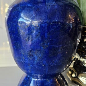 Könnte beinhalten: Eine blaue Vase aus Lapislazuli-Stein. Die Vase hat einen runden Körper und einen ausgestellten Boden. Die Oberfläche der Vase ist mit kleinen, quadratischen Lapislazuli-Stücken bedeckt.