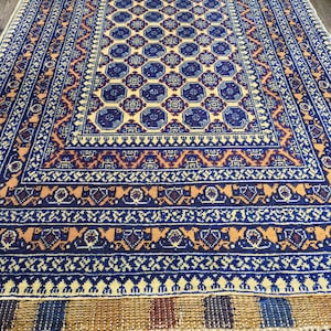 Könnte beinhalten: Ein traditioneller persischer Teppich mit cremefarbenem Hintergrund und komplizierten geometrischen Mustern in Blau, Rot und Orange. Der Teppich hat einen Fransenrand.