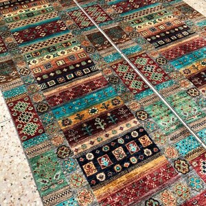 K&ouml;nnte beinhalten: Zwei farbenfrohe gemusterte Teppiche mit geometrischen und floralen Mustern in Rot-, Blau-, Gr&uuml;n- und Goldt&ouml;nen. Die Teppiche liegen nebeneinander auf einem gefliesten Boden.