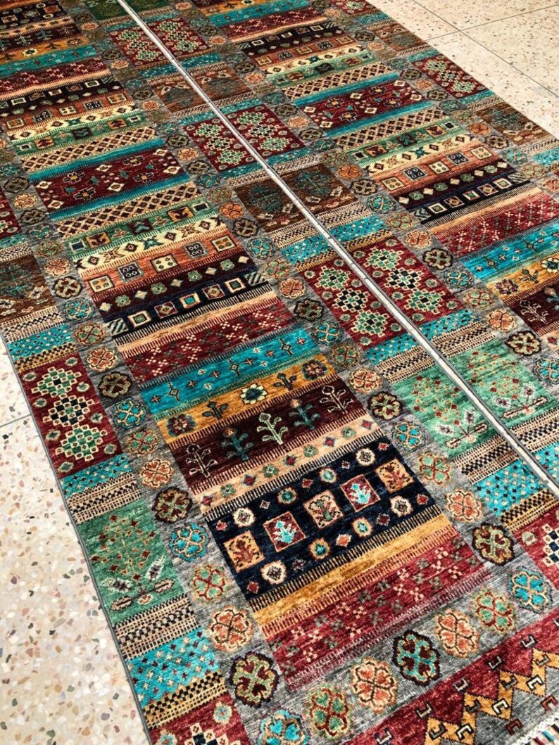 K&ouml;nnte beinhalten: Zwei farbenfrohe gemusterte Teppiche mit geometrischen und floralen Mustern in Rot-, Blau-, Gr&uuml;n- und Goldt&ouml;nen. Die Teppiche liegen nebeneinander auf einem gefliesten Boden.