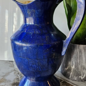 May include: A blue, ceramic pitcher with a wide mouth and a handle. The pitcher is decorated with a mosaic of blue and white tiles.