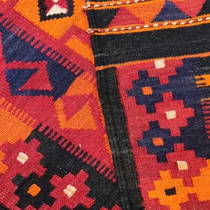 May include: A red, orange, black, and white patterned rug with a fringe border. The rug is woven with a geometric design.