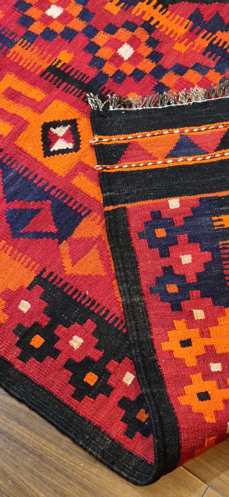 May include: A red, orange, black, and white patterned rug with a fringe border. The rug is woven with a geometric design.