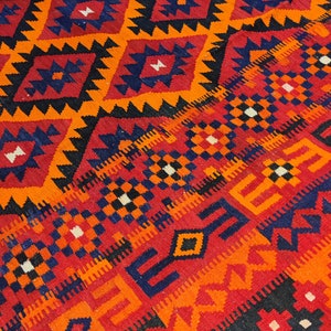 May include: A colorful rug with a geometric pattern in shades of red, orange, black, and blue. The rug has a traditional design with intricate details.