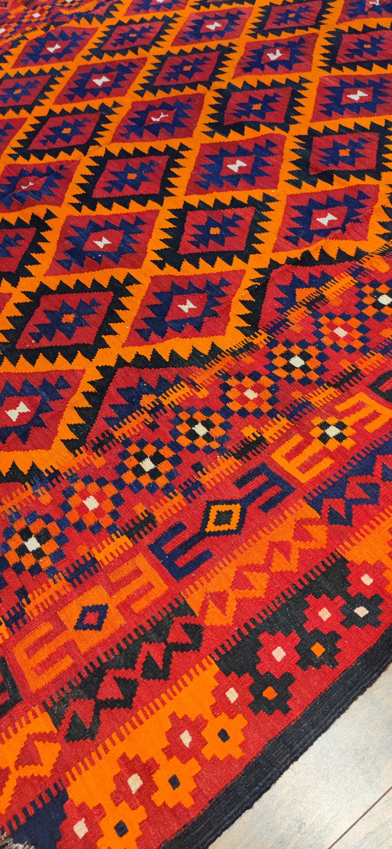 May include: A colorful rug with a geometric pattern in shades of red, orange, black, and blue. The rug has a traditional design with intricate details.