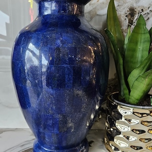 Könnte beinhalten: Eine blaue und goldene Keramikvase mit geometrischem Muster. Die Vase steht auf einer weißen Marmorfläche.