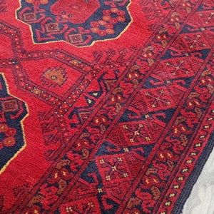 Könnte beinhalten: Ein roter Teppich mit traditionellem persischem Design. Der Teppich hat einen dunkelblauen Rand und komplizierte Muster in Rot-, Blau- und Goldtönen.