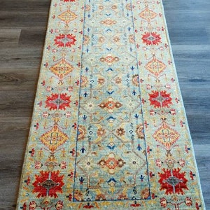 Könnte beinhalten: Ein langer, rechteckiger Teppich mit einem geometrischen Muster in Blau, Rot, Gelb und Weiß. Der Teppich hat einen Fransenrand.