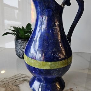 Könnte beinhalten: Eine blaue und grüne dekorative Kanne aus Lapislazuli und Malachit. Die Kanne hat eine breite Öffnung und einen Henkel. Sie steht auf einer weißen Marmorfläche.