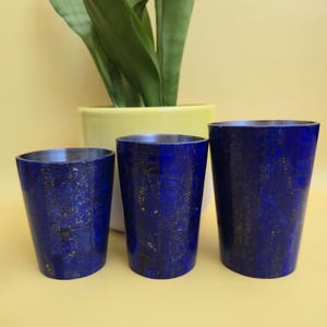 Könnte beinhalten: Drei blaue Lapis-Lazuli-Becher in verschiedenen Größen. Die Becher haben eine dunkelblaue Farbe mit Goldflocken. Die Becher sind in einer Reihe angeordnet, mit einer Pflanze in einem gelben Topf im Hintergrund.