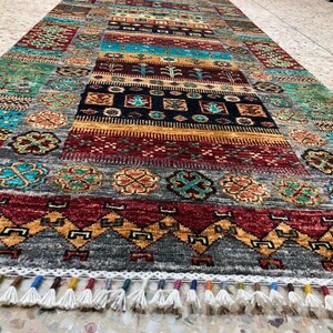 K&ouml;nnte beinhalten: Ein bunter Teppich mit geometrischem Muster und Fransen. Der Teppich hat eine Vielzahl von Farben, darunter Rot, Blau, Gr&uuml;n und Gelb. Der Teppich ist aus Wolle und hat eine weiche Textur.
