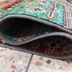 K&ouml;nnte beinhalten: Nahaufnahme eines bunten Teppichs mit einem grauen Rand. Der Teppich ist in der Mitte gefaltet und zeigt das komplizierte Muster und die Textur des Stoffes.